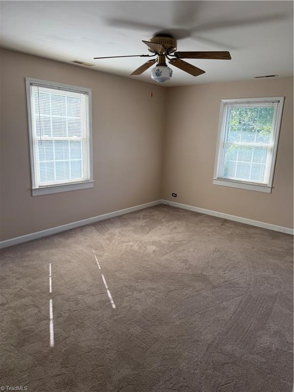 Empty bedroom with beige carpet, two windows with blinds, and a ceiling fan.