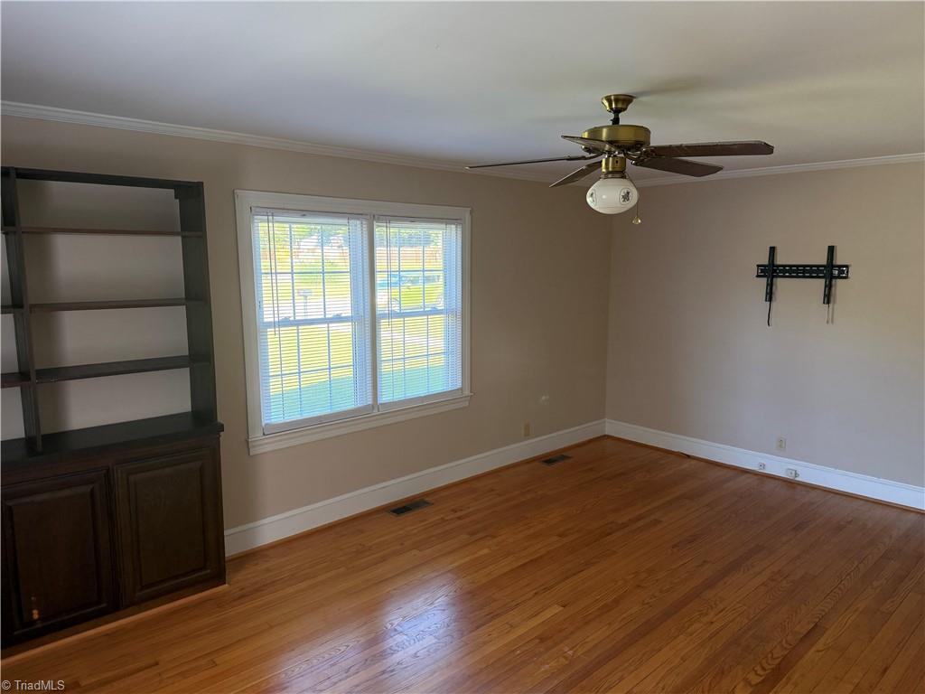 Empty room with hardwood floors, a ceiling fan, and built-in shelving beside a window.
