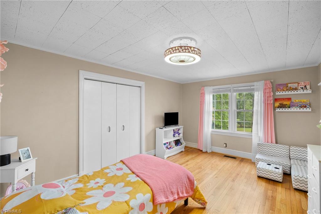 Bedroom with two beds, hardwood floors, and a wide window overlooking greenery.