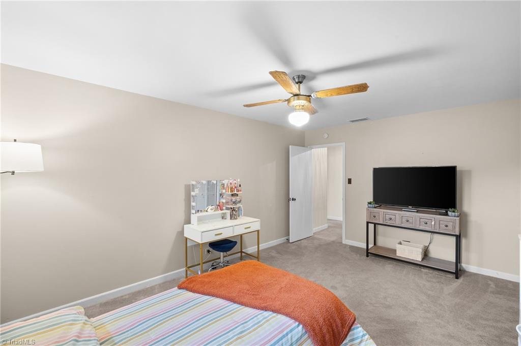 Bedroom with striped bedding, an orange throw, ceiling fan, vanity, and television.