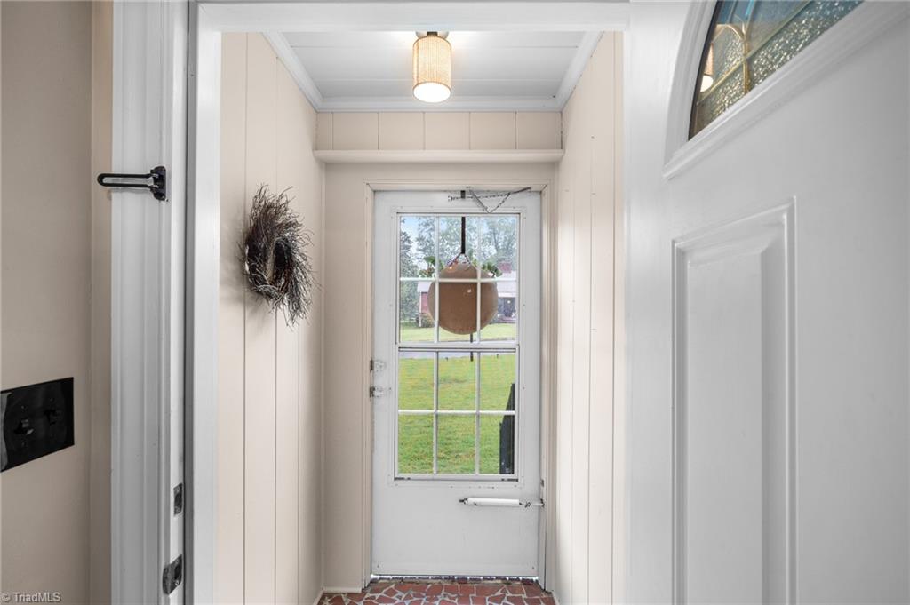 Bright white entryway with a wreath, patterned tile floor, and glass-paneled door overlooking a lawn.