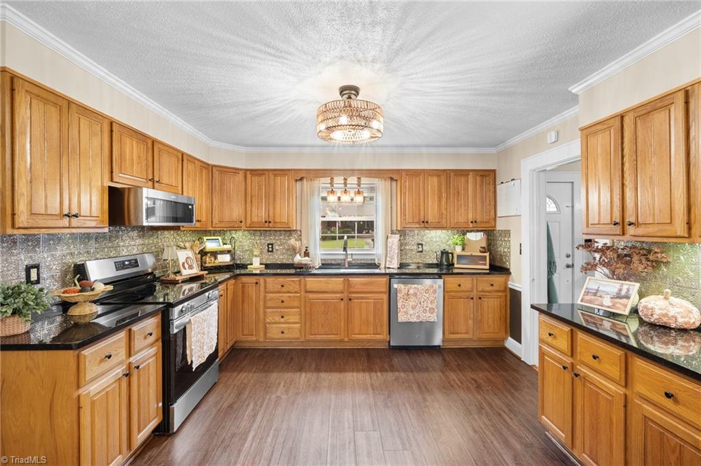 Kitchen with honey-colored wood cabinets, black countertops, and a stainless steel range.
