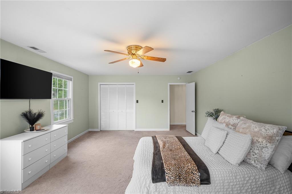 Furnished bedroom with pale green walls, a white bed, ceiling fan, and wall-mounted television.