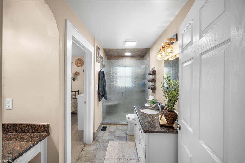 Bathroom with a frosted-glass walk-in shower and white vanity with dark granite countertop.
