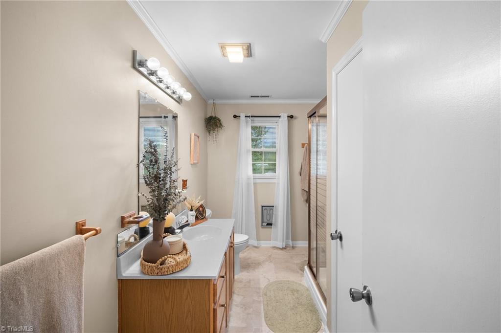 Bathroom with a wood vanity, glass shower enclosure, and a curtained window.