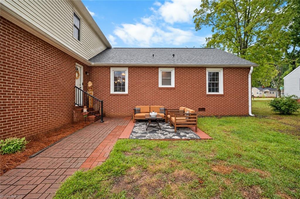 Brick home’s rear patio with outdoor seating, a brick walkway, and lawn.