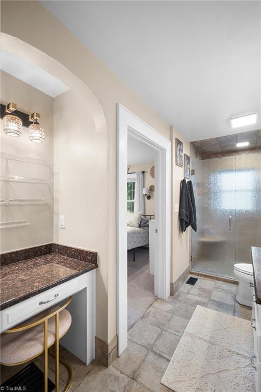 Bathroom with a granite vanity, arched alcove, and glass-enclosed shower.