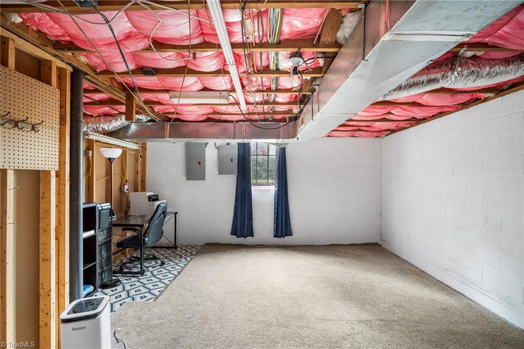 Basement with carpeted floor, exposed ceiling insulation, and a small desk area.