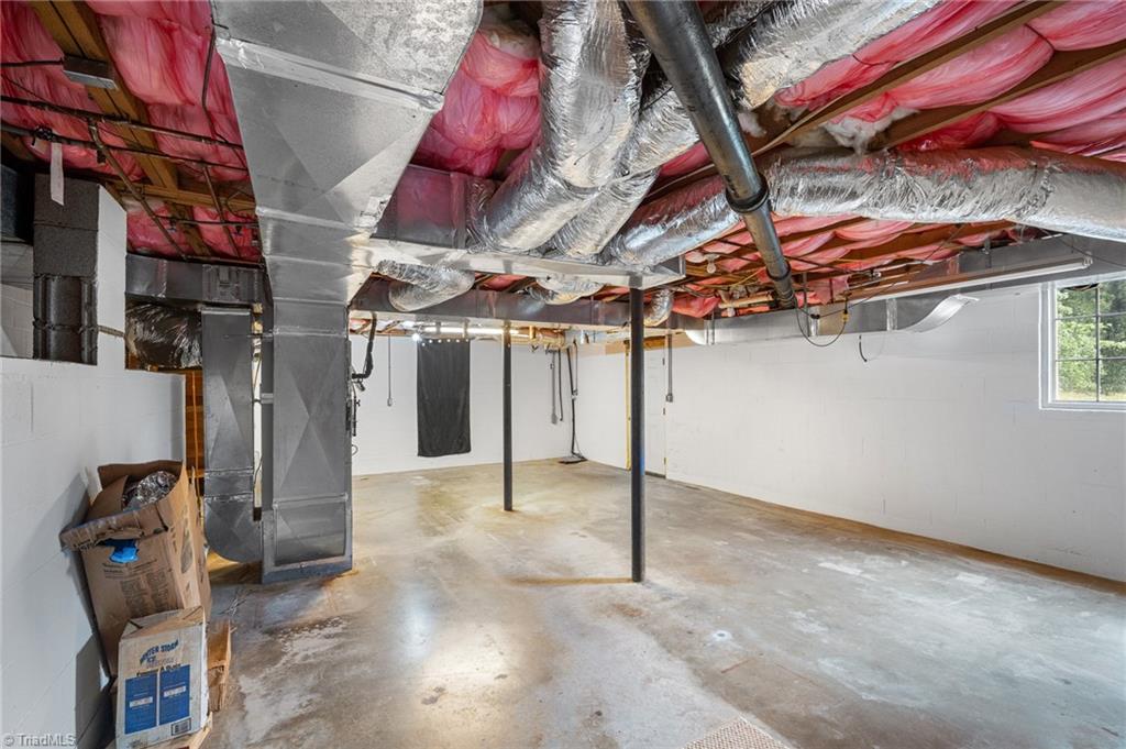 Unfinished basement with exposed insulation and HVAC ducts over a concrete floor.