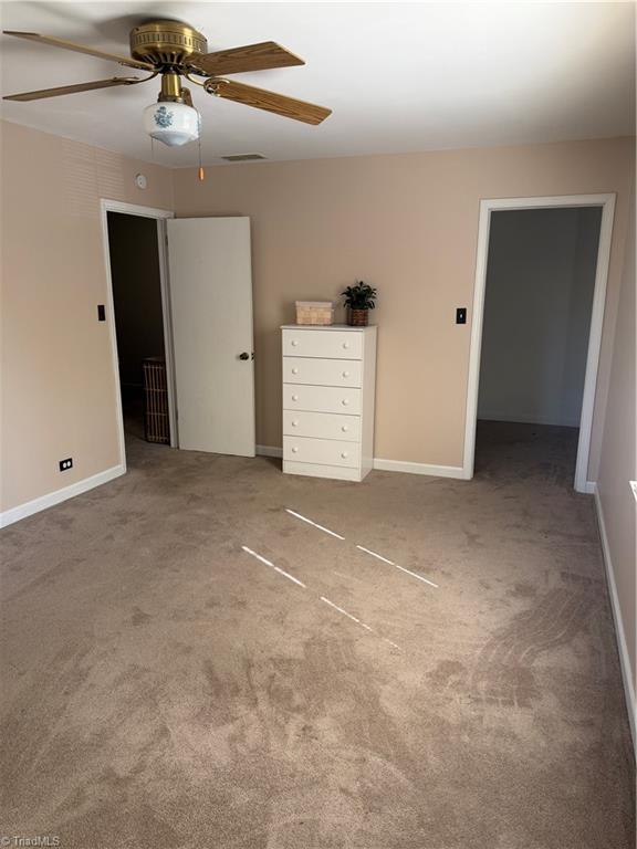 Beige carpeted bedroom with a brass ceiling fan, white dresser, and two open doorways.