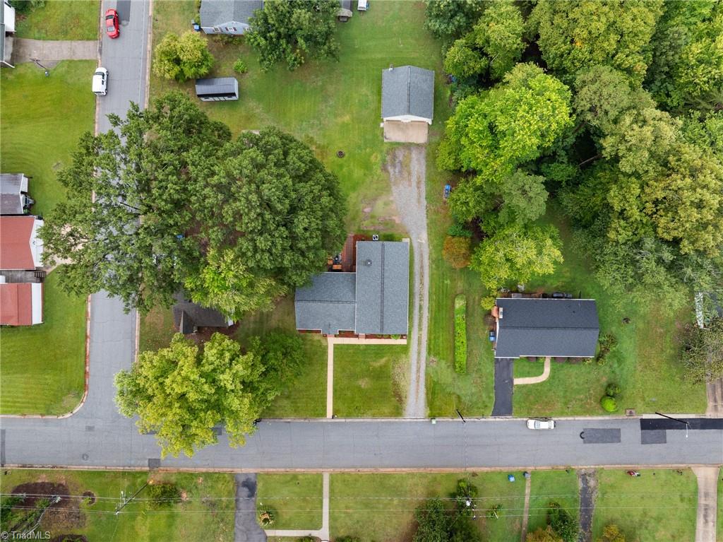 Aerial view of a house on a leafy lot with a gravel driveway and detached outbuilding.
