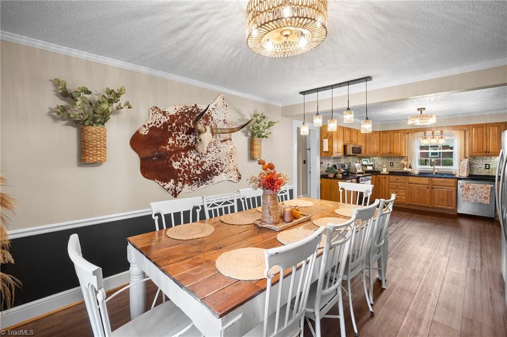 Dining room with a rustic wood table and white chairs opening into a wood-cabinet kitchen.