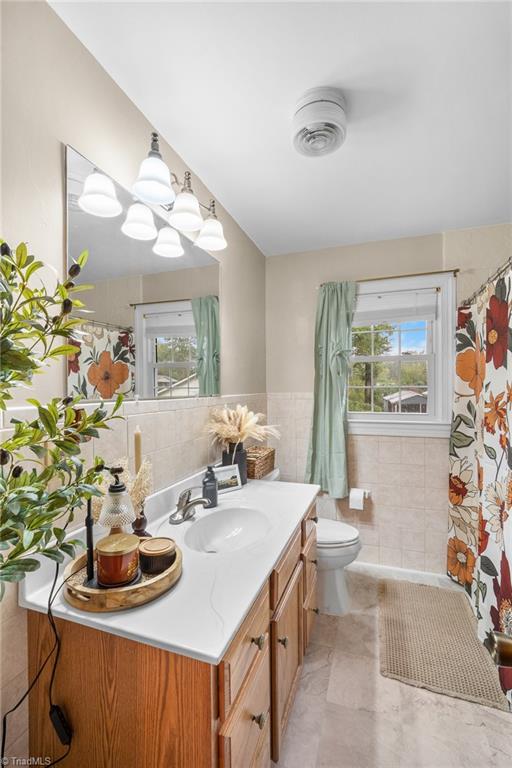 Bathroom with a wood vanity, floral shower curtain, and window framed by pale green curtains.