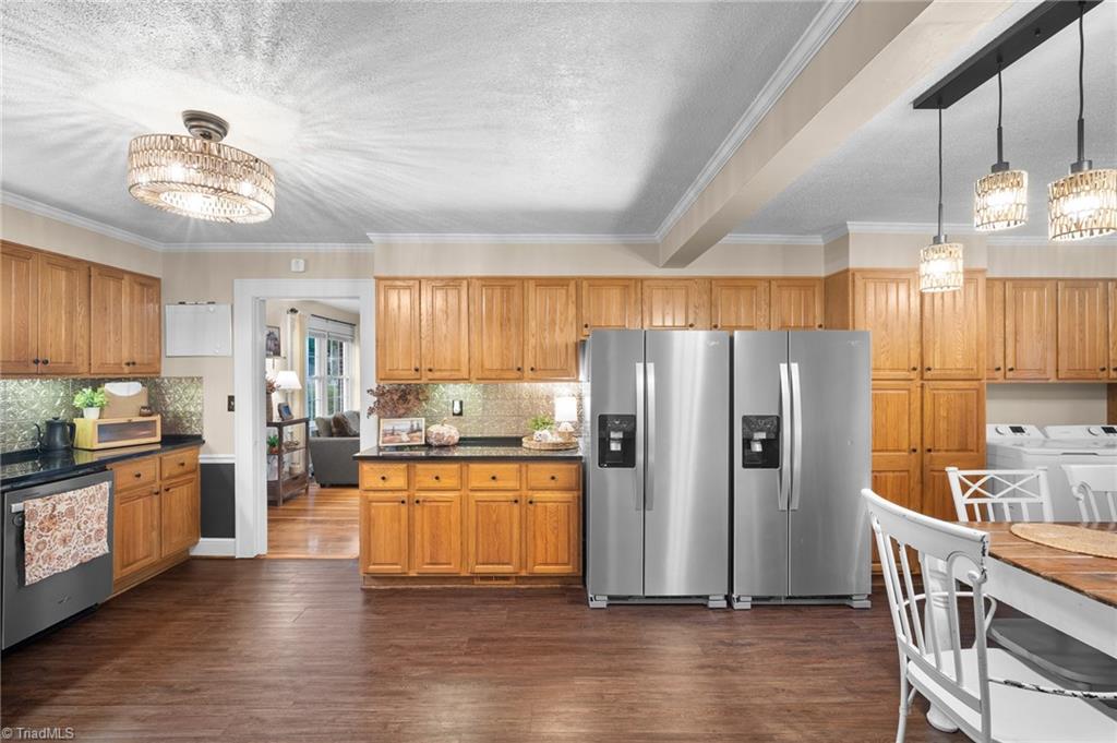 Kitchen with honey-toned cabinets, stainless steel refrigerators, and a dining table beneath pendant lights.