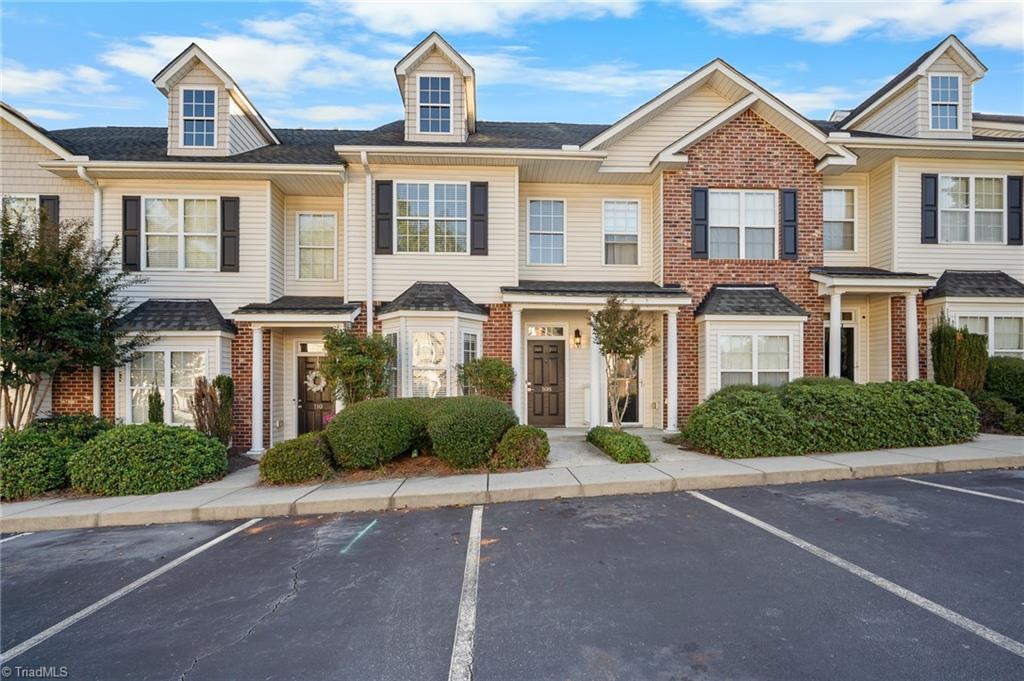 Townhouse exterior with beige siding, red-brick accents, dormer windows, and landscaped shrubs.