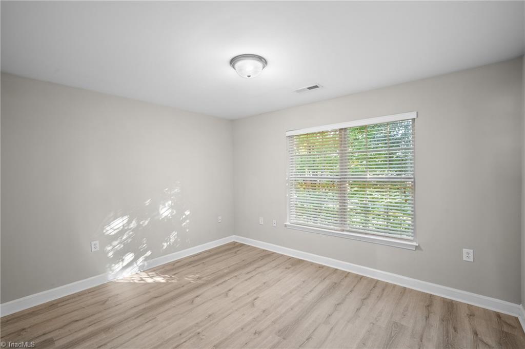 Empty bedroom with light wood-look flooring and a wide window with white blinds.
