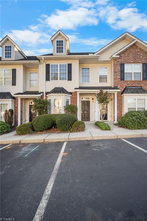 Townhouse exterior with beige siding, brick accents, landscaped shrubs, and parking spaces in front.