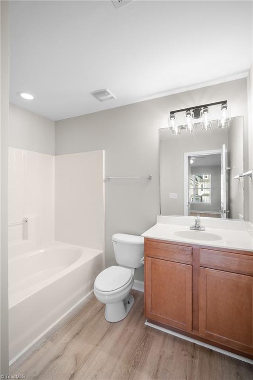 Bathroom with a white bathtub, toilet, and wood vanity beneath a large mirror.
