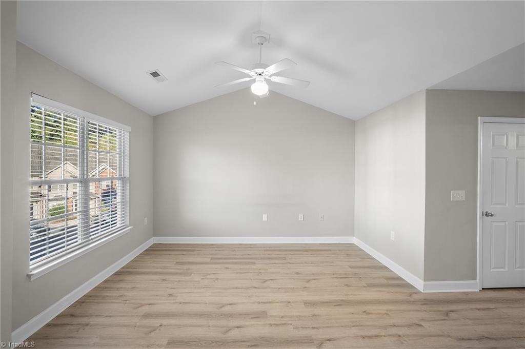 Empty room with wood-look flooring, a wide window with blinds, and a ceiling fan.