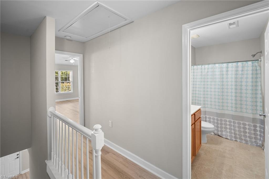 Upstairs landing with white railing beside a bathroom with a teal-and-gray circle-patterned shower curtain.