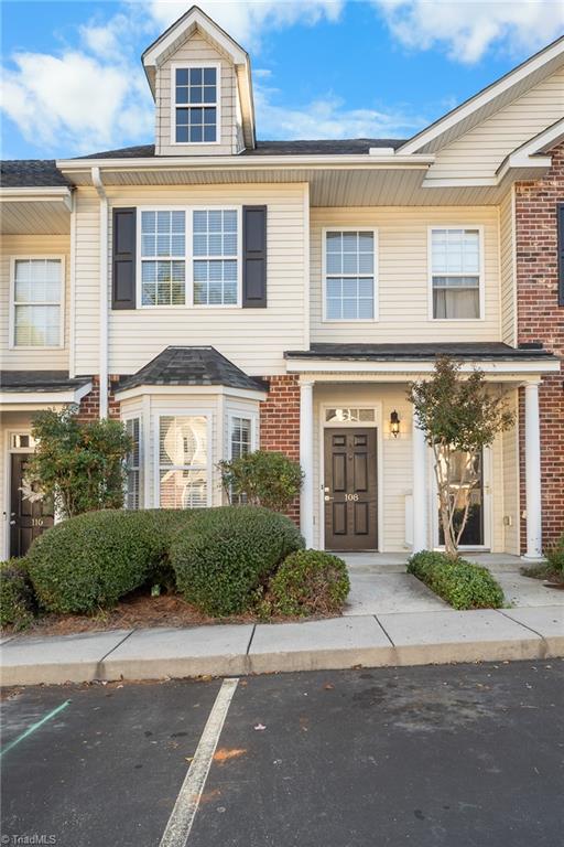 Attached two-story home with cream siding, brick accents, a roof dormer, and landscaped entrance.