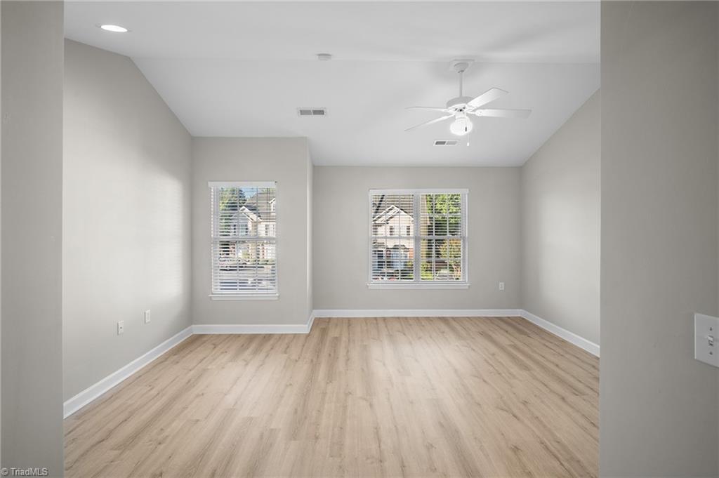 Empty room with light wood-look flooring, two windows with blinds, and a ceiling fan.