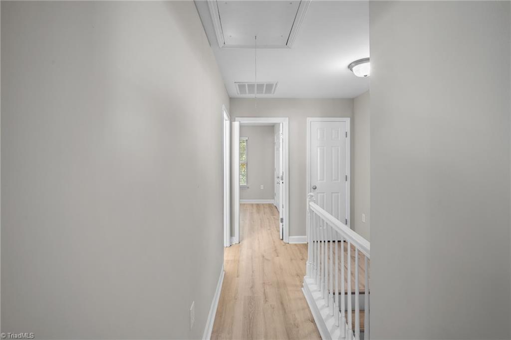 Upstairs hallway with light wood flooring, white stair railing, and multiple doorways.