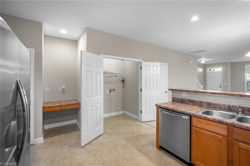 Kitchen with wood cabinets and stainless appliances, beside an open closet with a hanging rod.