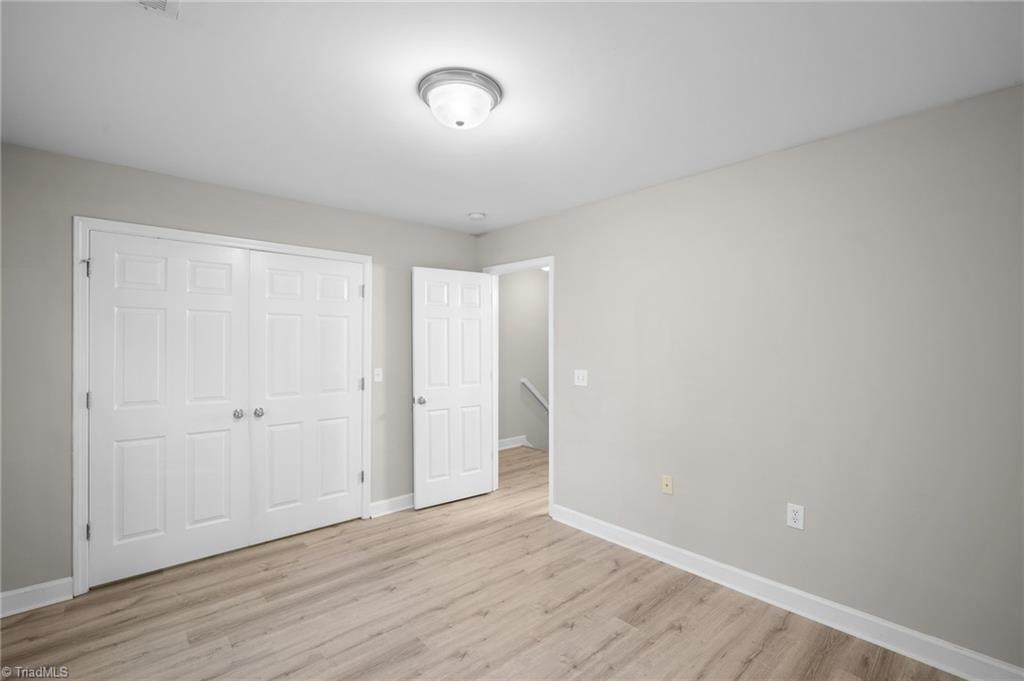 Vacant room with double closet doors, pale wood-look flooring, and an open doorway to the hall.