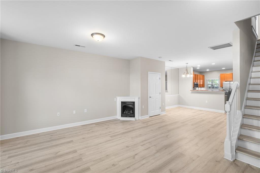 Open living area with light wood-look floors, a fireplace, staircase, and orange-toned kitchen cabinets.
