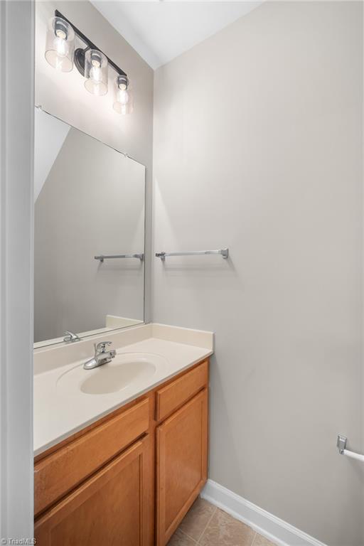 Bathroom vanity with wood cabinets, oval sink, large mirror, and three-light fixture.