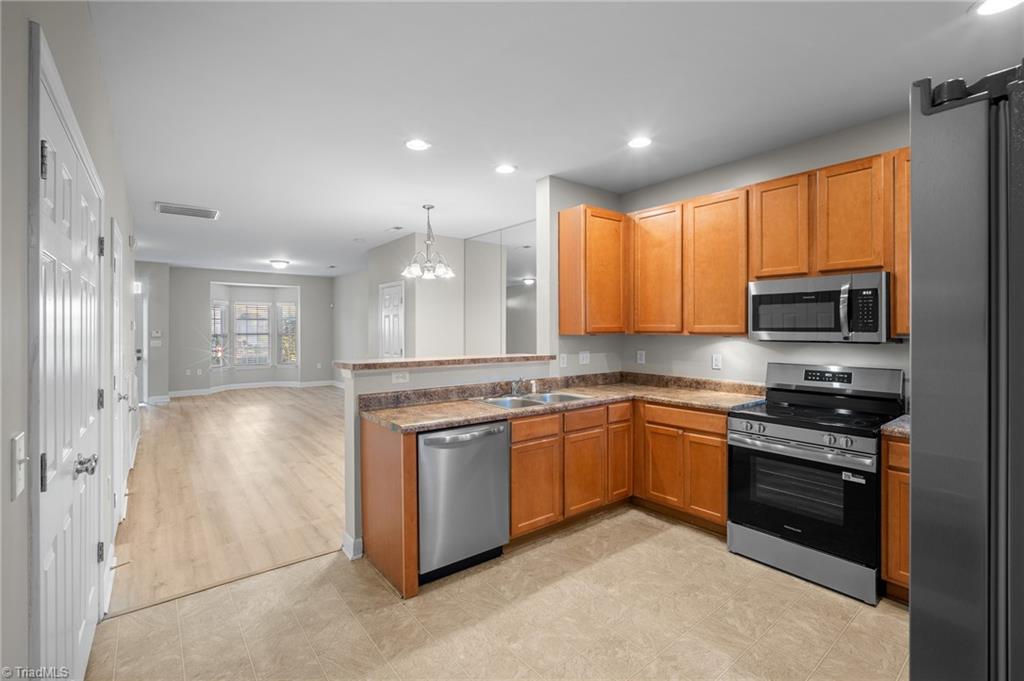 Unfurnished kitchen with warm wood cabinets, stainless steel appliances, and an open living area.