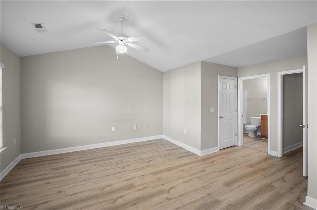 Vacant bedroom with wood-look flooring, a ceiling fan, and an adjoining bathroom.