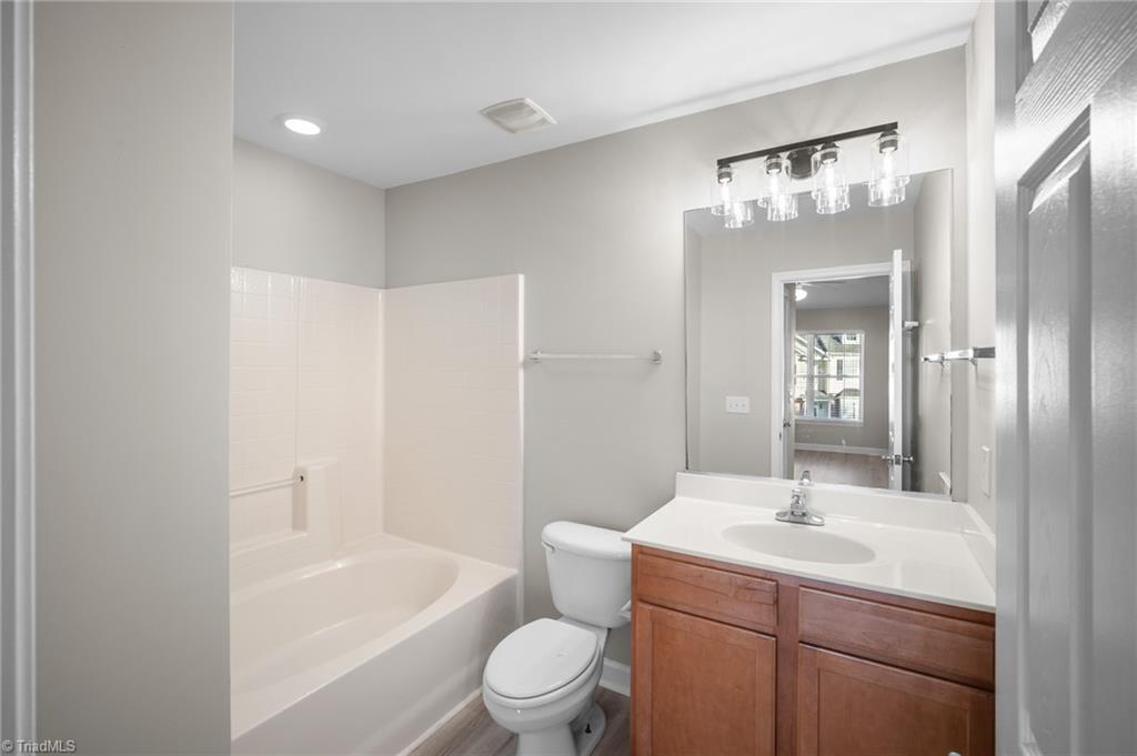 Bathroom with a white tub, toilet, and wooden vanity beneath a large mirror.