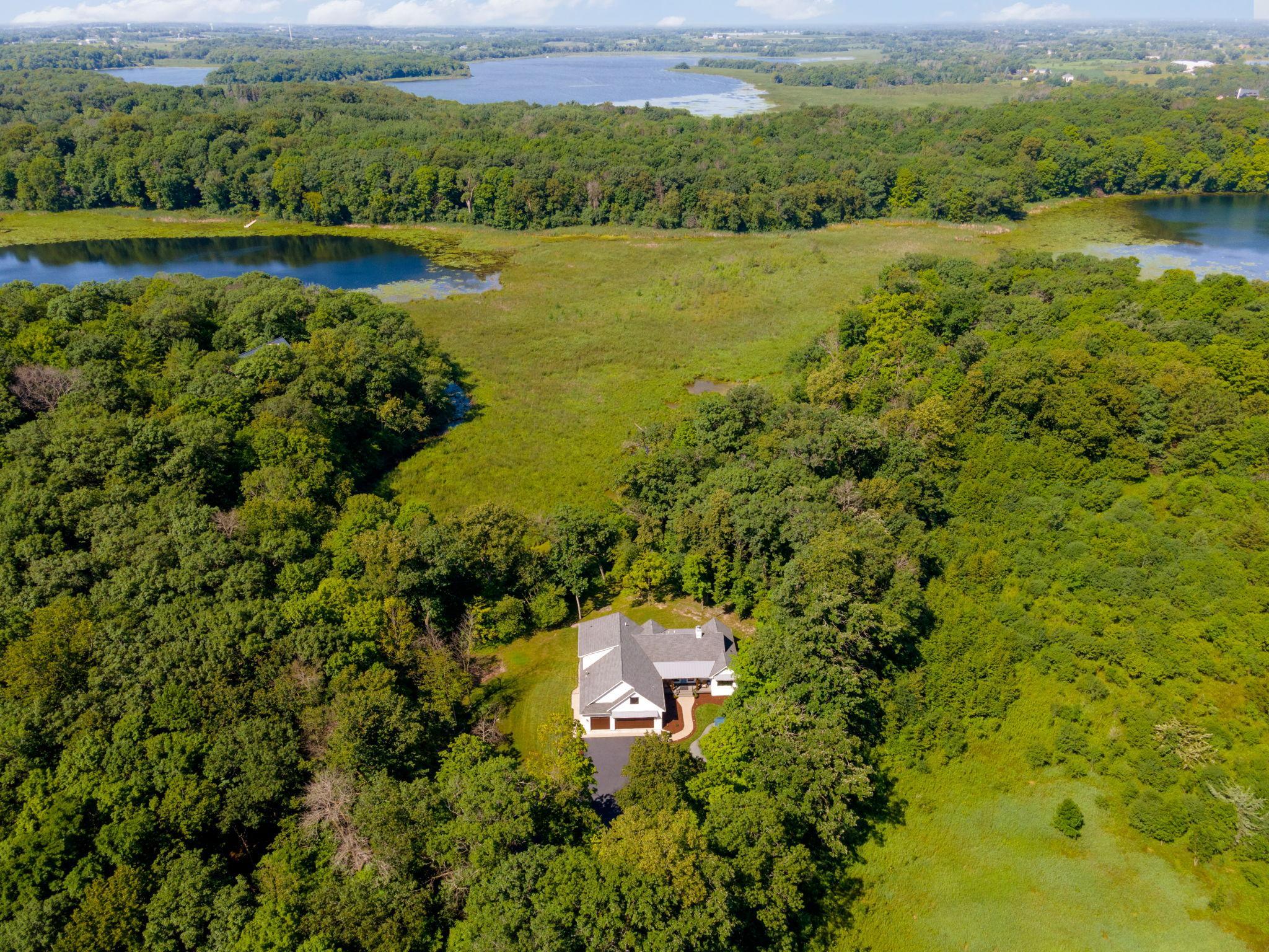 Aerial view of a house amid wooded grounds, wetlands, and lakes.