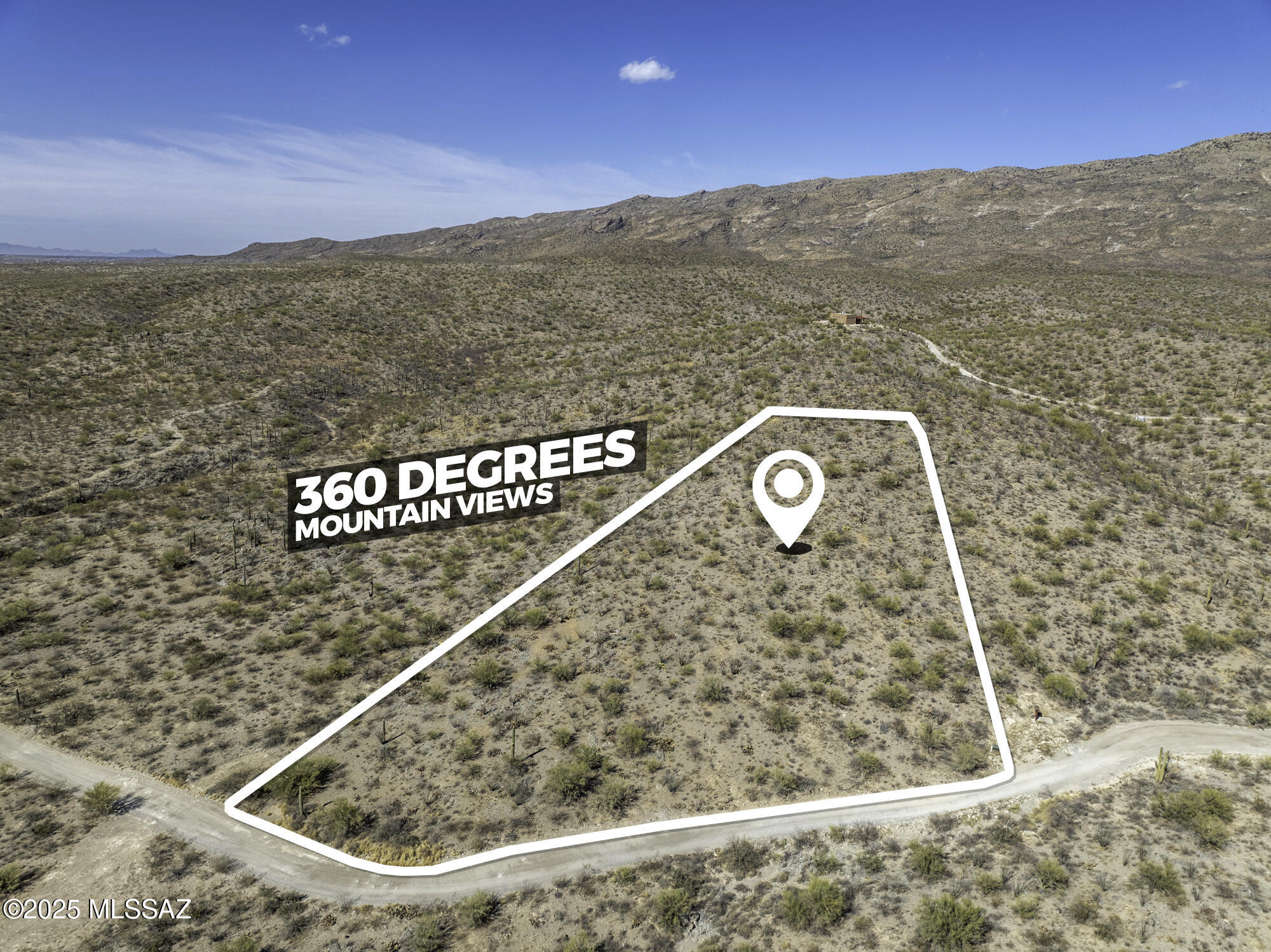 Aerial view of a scrub-covered desert parcel outlined beside a dirt road, with a rocky mountain ridge beyond.