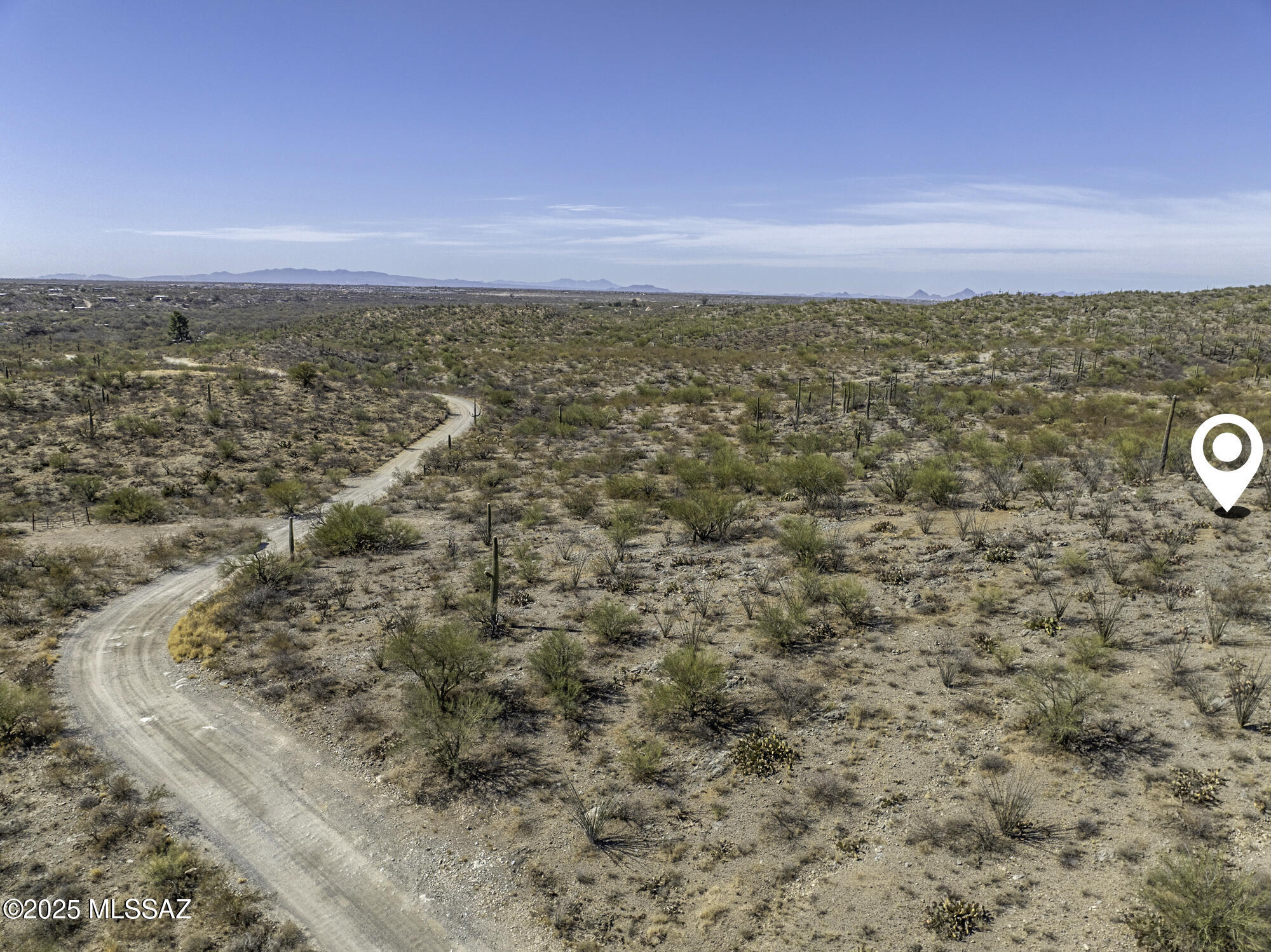 Aerial view of desert land with a winding dirt road, scattered saguaros, and distant mountains.