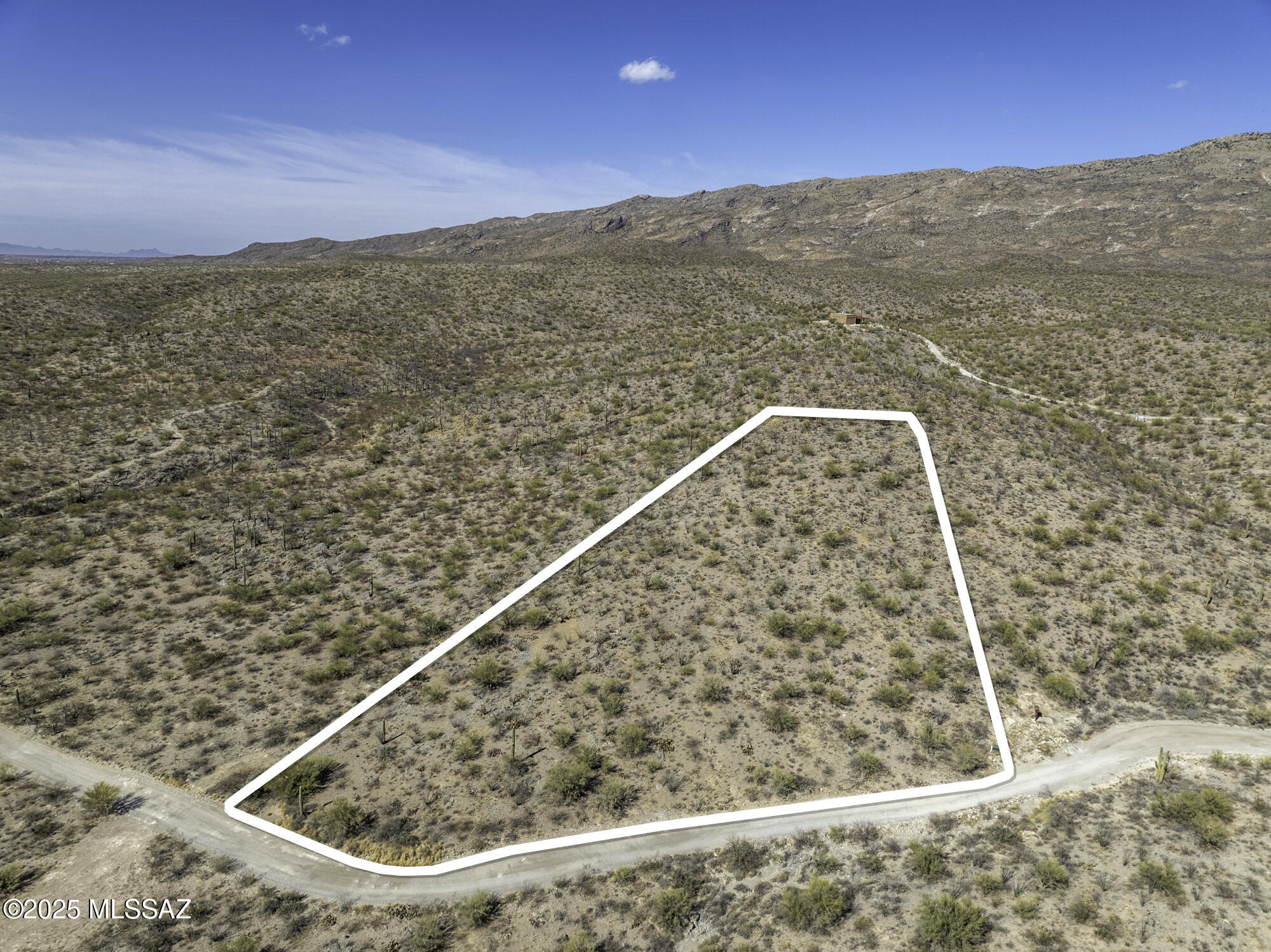 Aerial view of a white-outlined desert parcel beside a dirt road, with distant mountains.