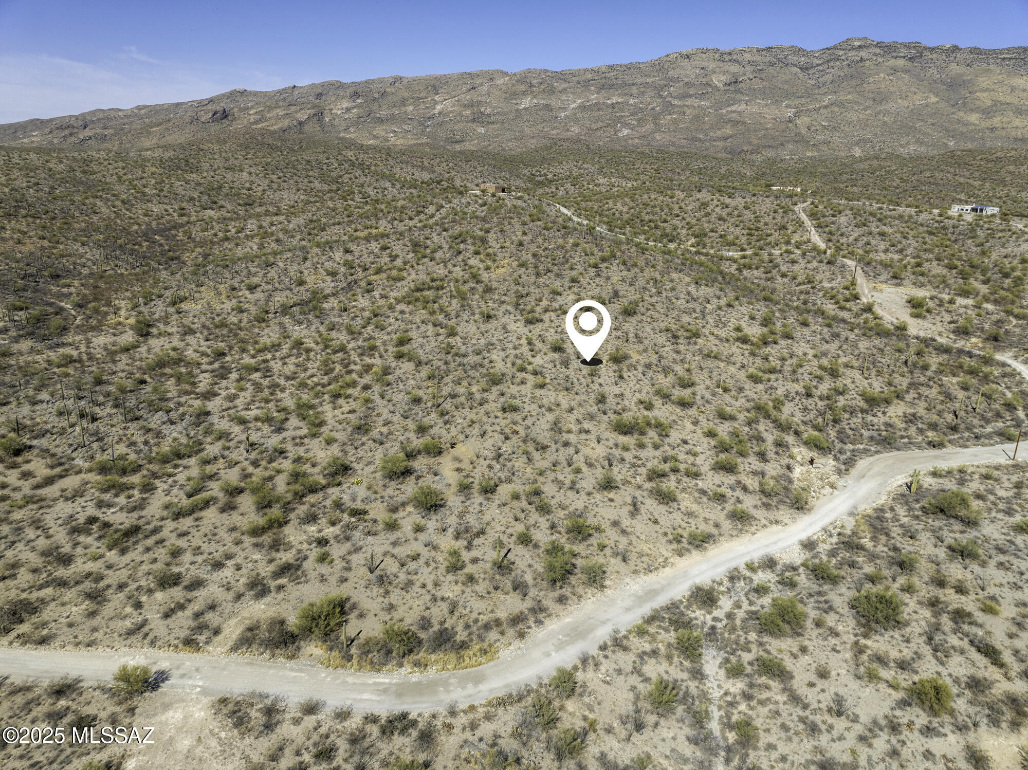 Aerial view of a desert parcel with a location marker, curving dirt road, and distant mountain ridge.