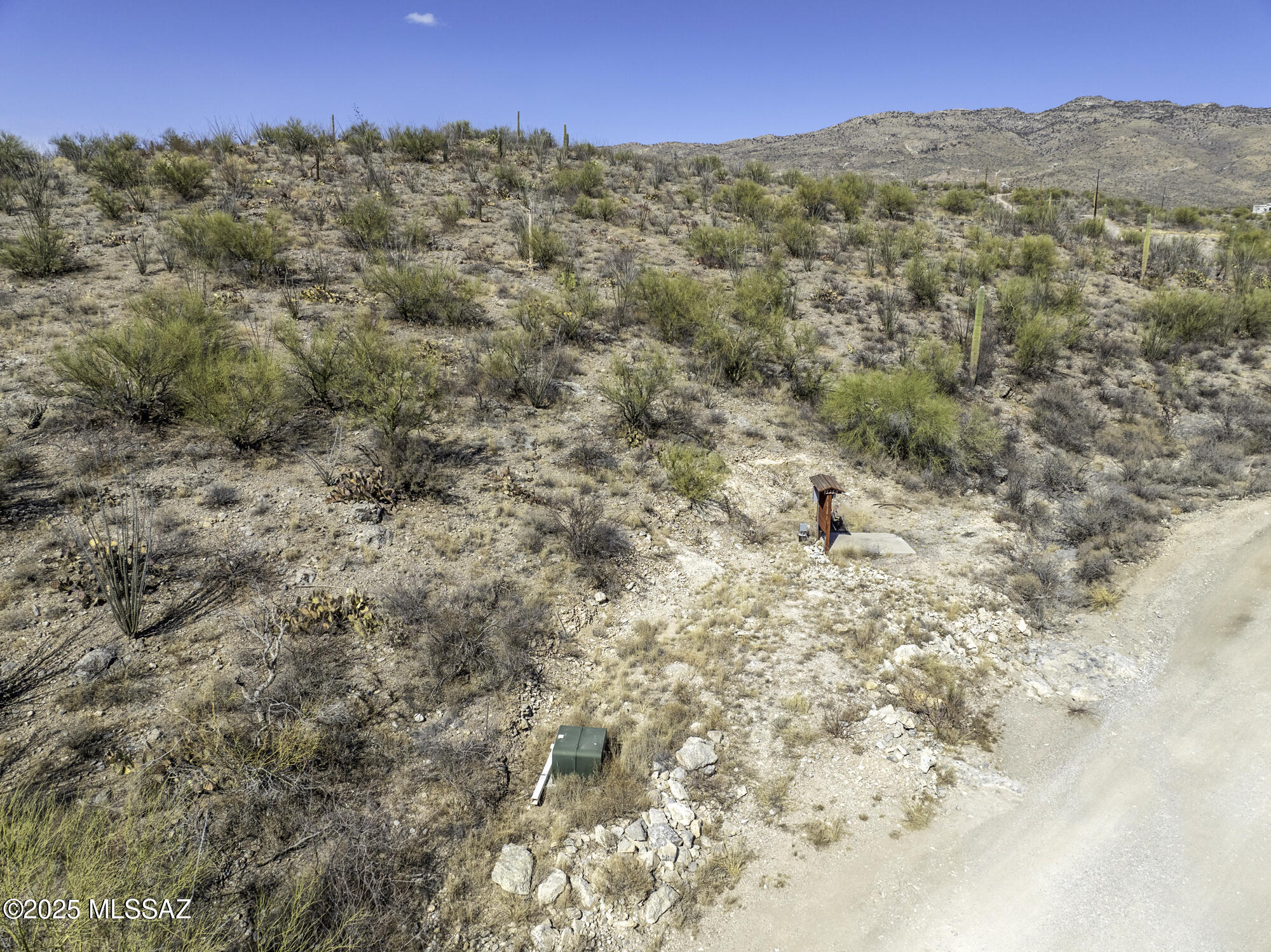 Desert property with scattered cacti, utility equipment, and mountains beyond.