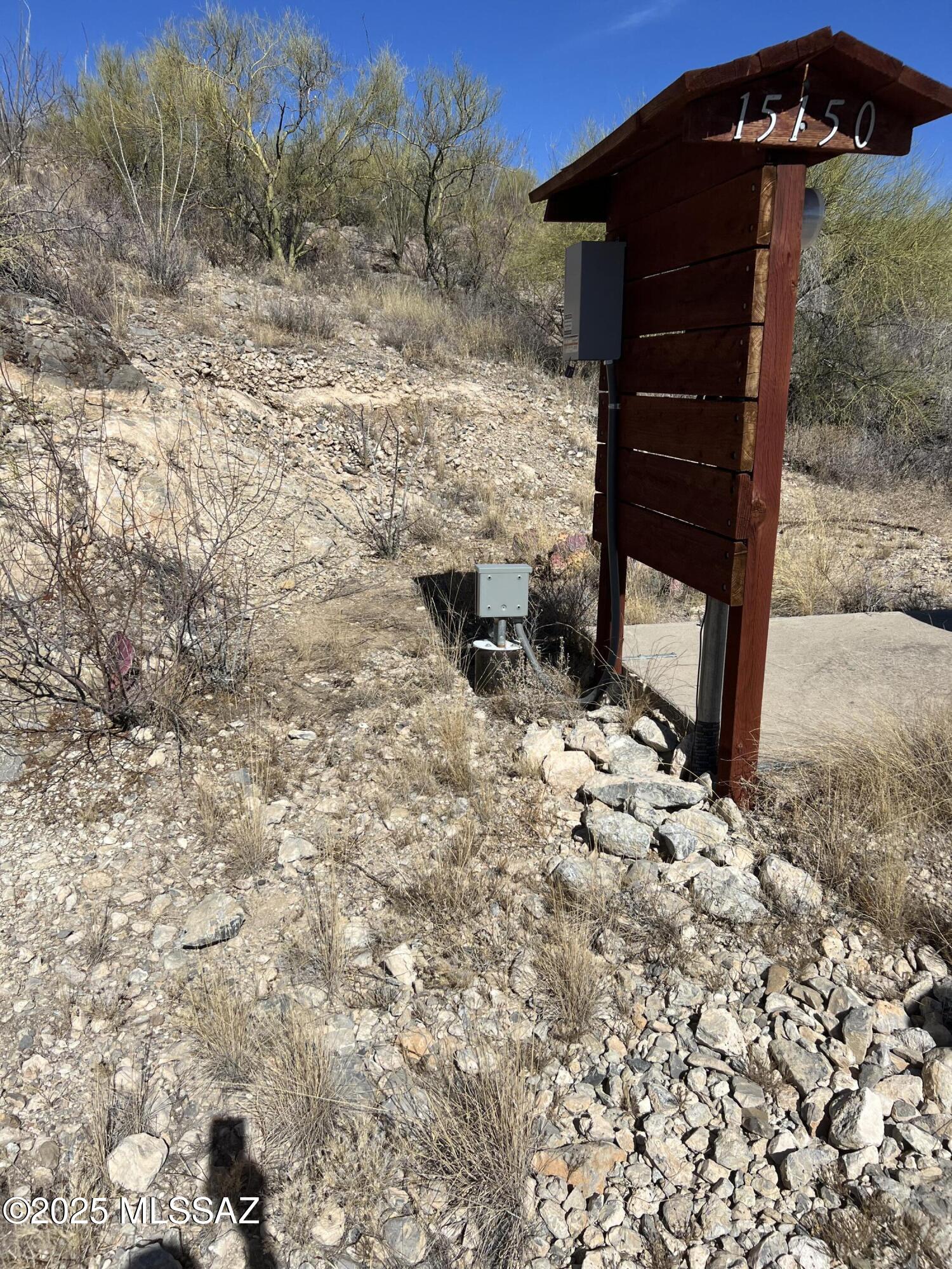 Wooden entrance sign marked 15150 beside a concrete driveway and rocky desert hillside.