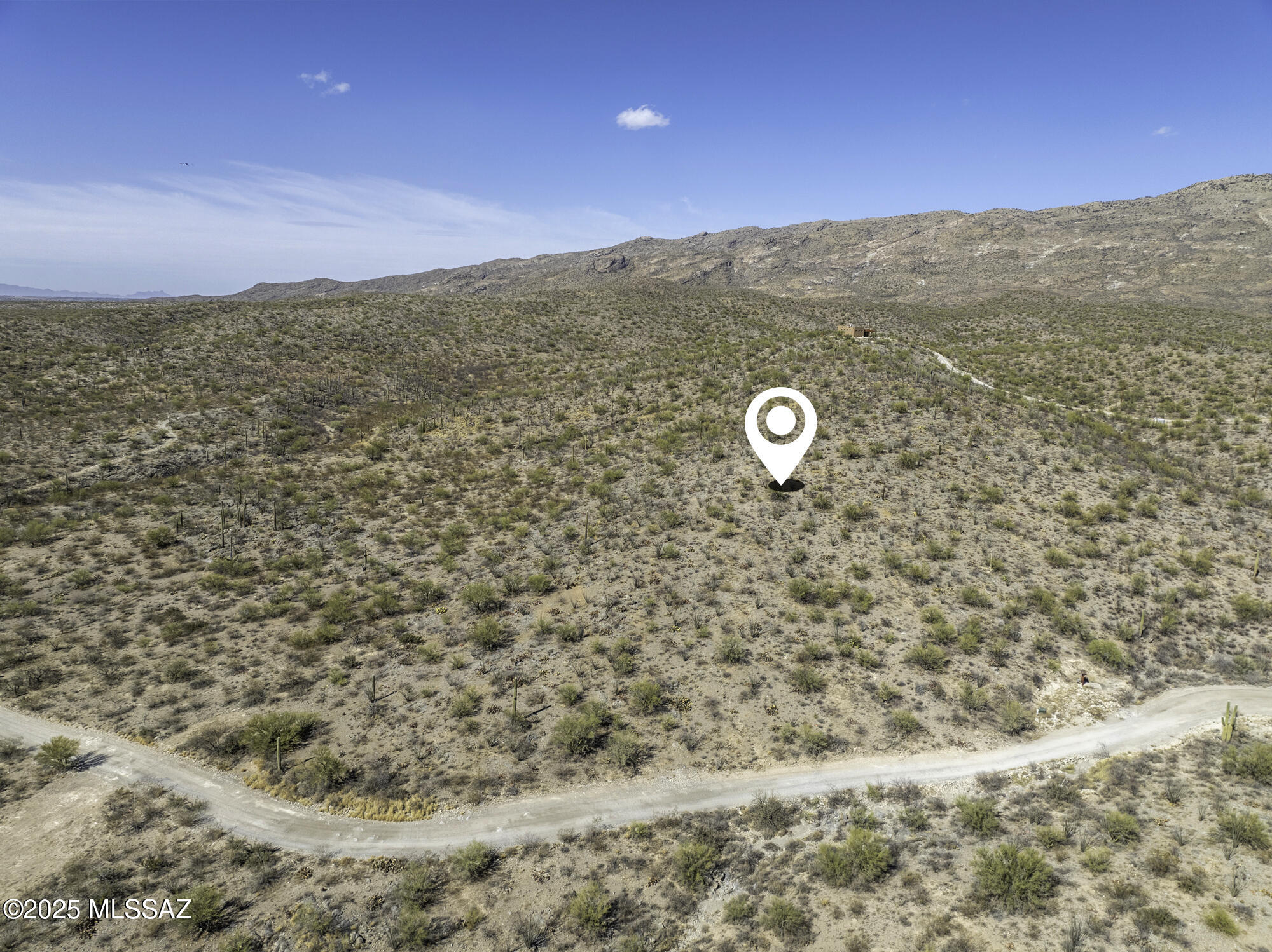 Aerial view of vacant desert land with a winding dirt road and rocky mountains behind it.
