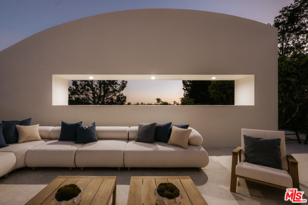 Outdoor patio lounge with a long sectional sofa beneath a horizontal window in a curved stucco wall.