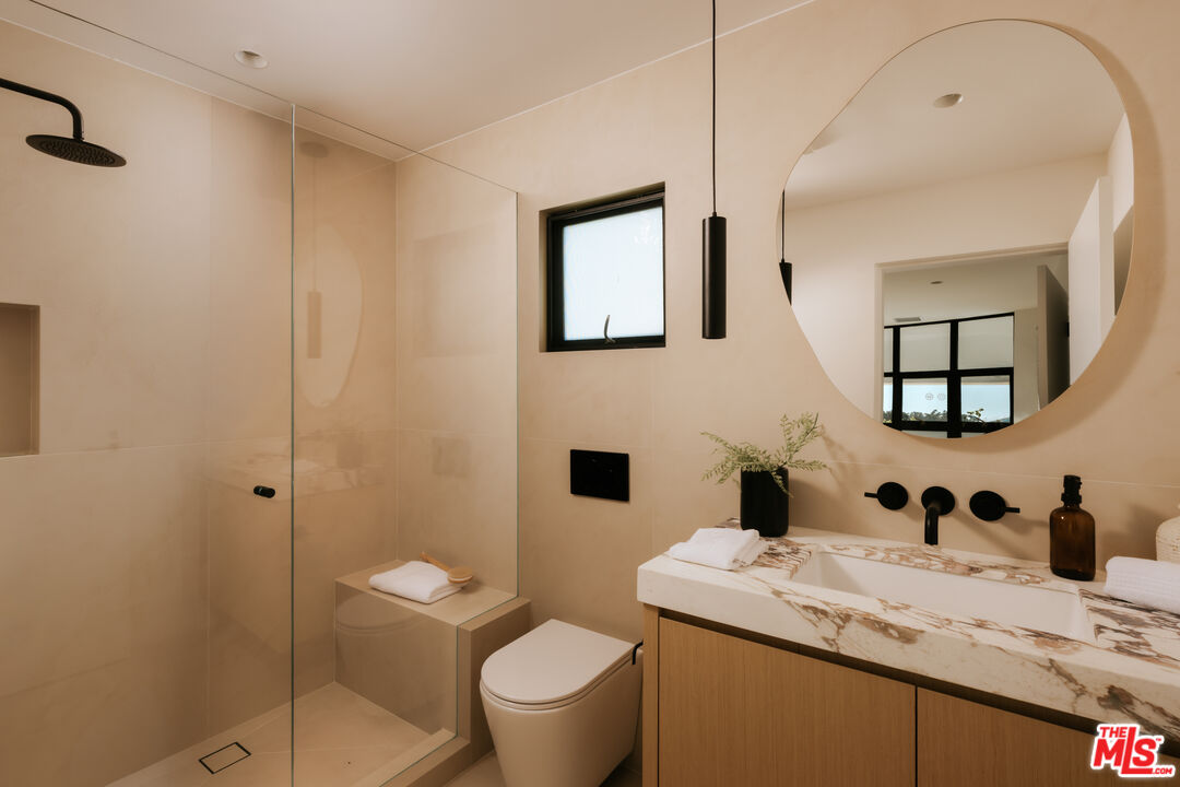 Modern bathroom with a glass walk-in shower and wood vanity beneath a large round mirror.