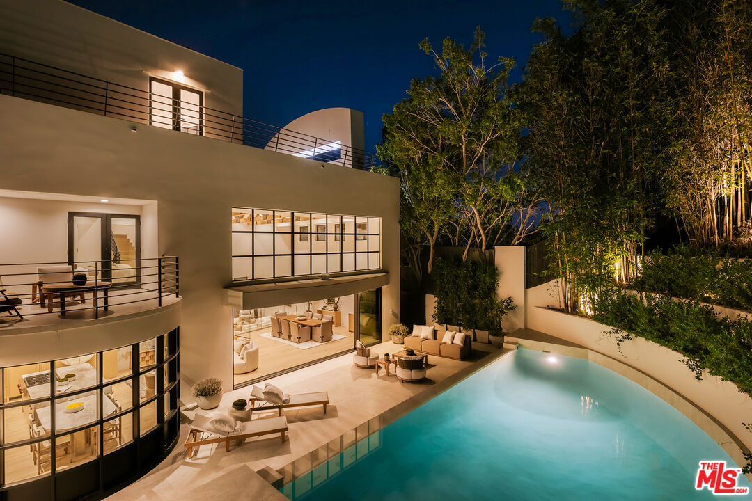 Modern two-story home with a glass-walled patio and illuminated pool at night.