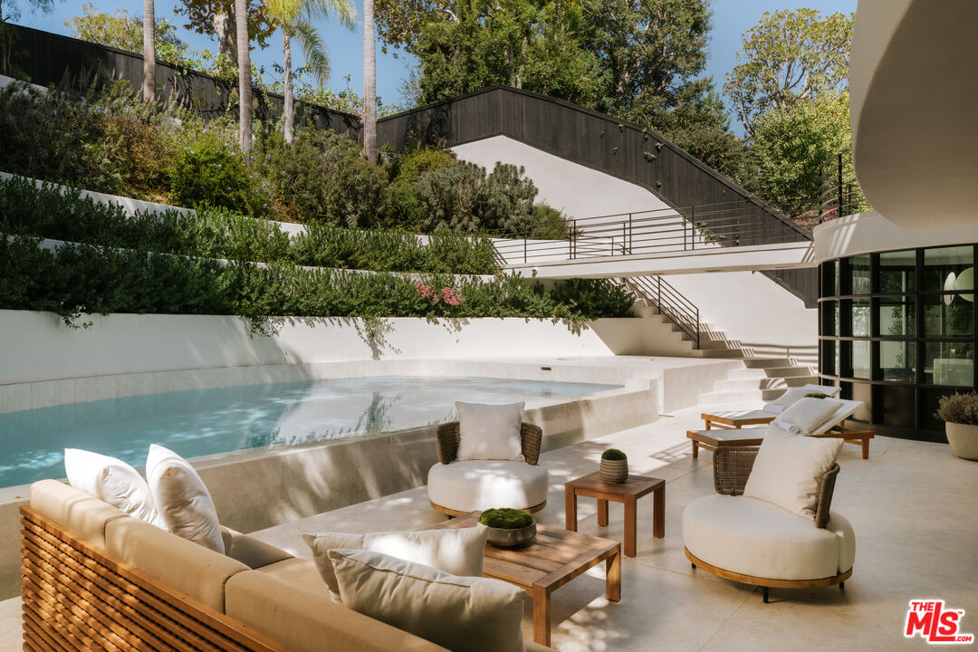 Outdoor pool and patio with cream lounge seating, landscaped walls, and broad exterior stairs.