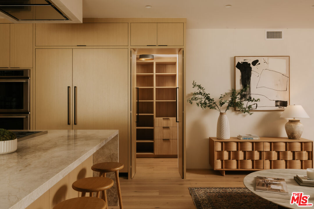 Modern kitchen with light oak cabinetry, marble island, and adjoining living area with abstract art.