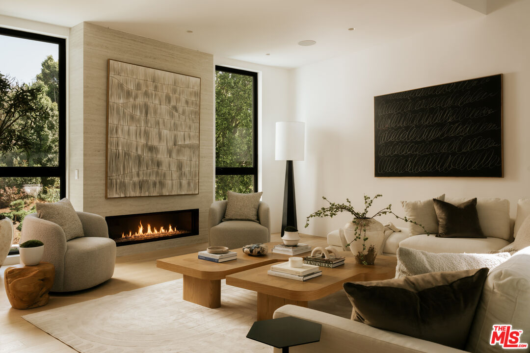 Contemporary living room with a linear fireplace, tall windows, and sculptural wood coffee tables.