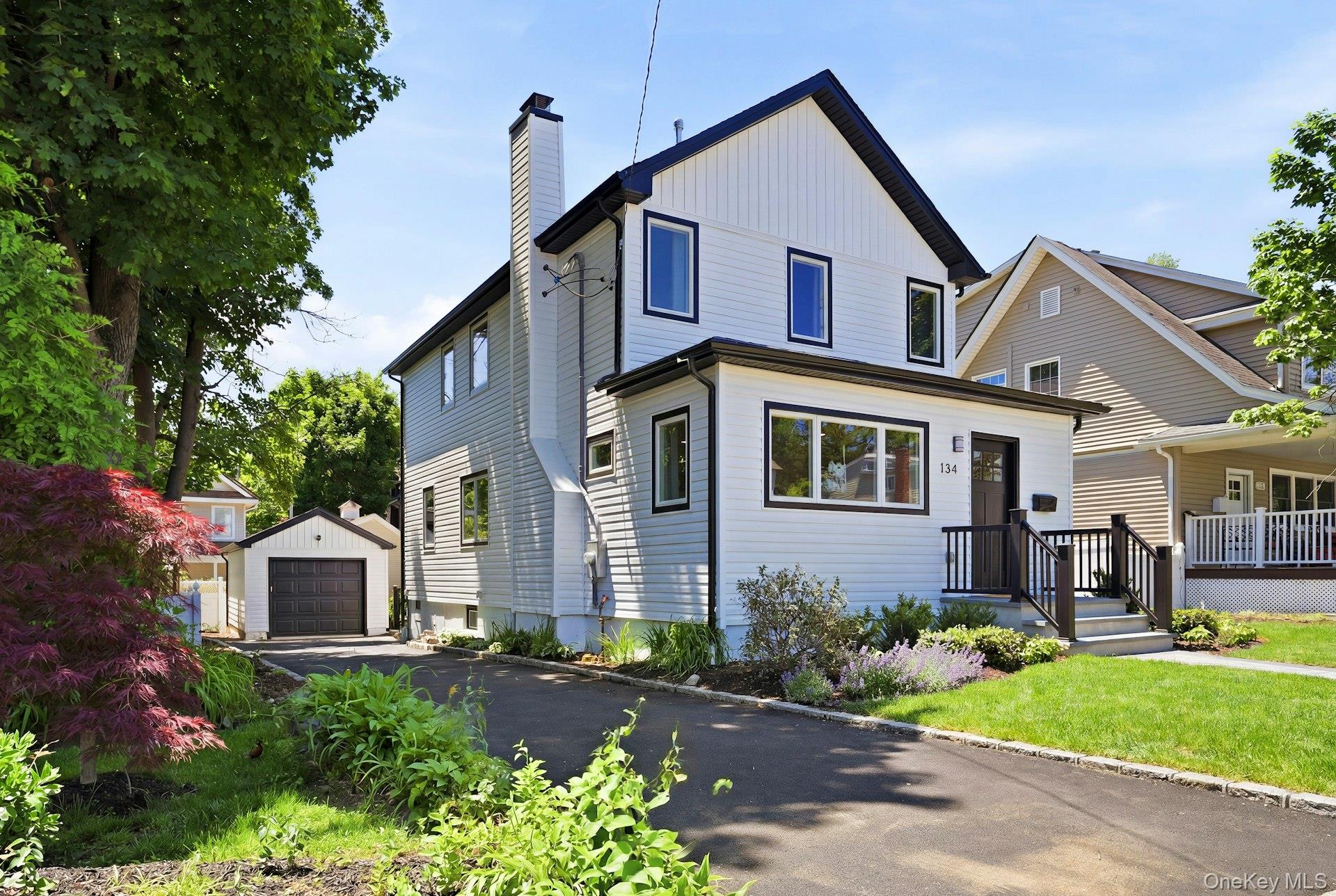 White two-story house with dark trim, a covered porch, and a landscaped front yard.