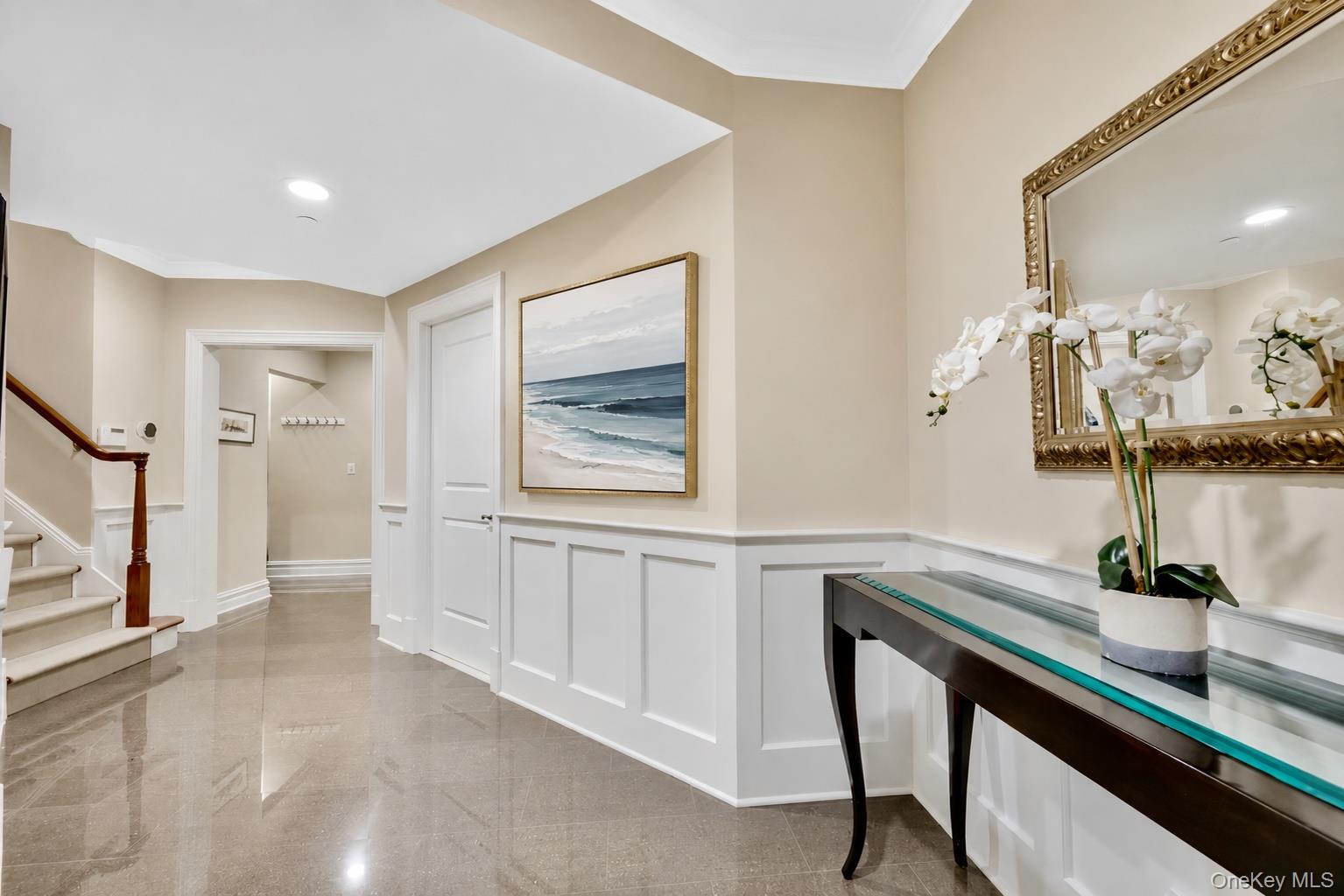 Entry hall with glossy tile floors, paneled walls, a staircase, and a glass-top console table.